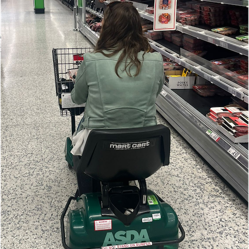 Charlotte Croft in an Asda mobility scooter driving down a shopping aisle with her back to the camera