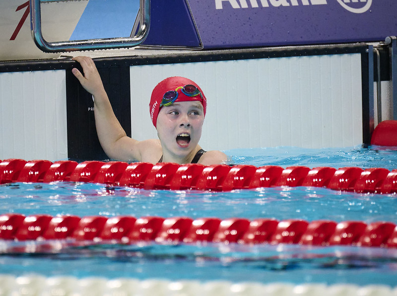 Iona Winnifrith in the swimming pool wearing a red swimming hat and goggles looking in utter shock after finishing the race 