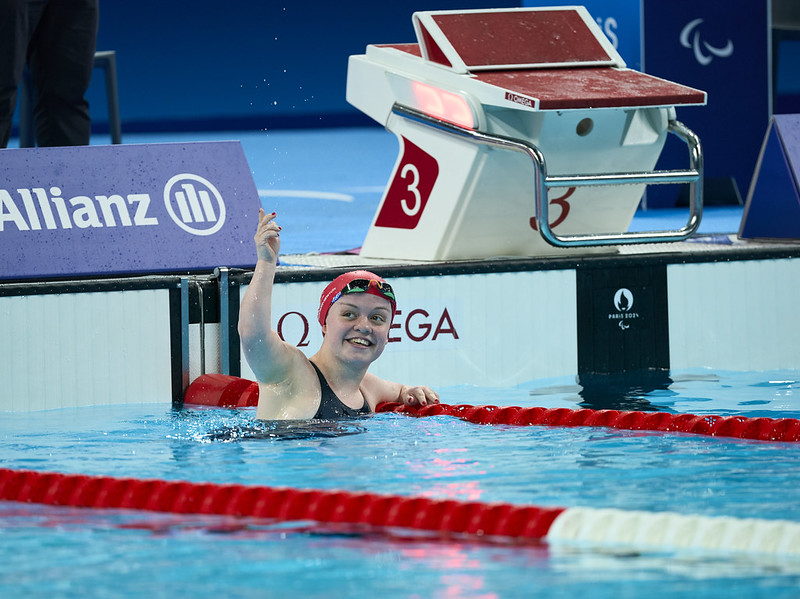 Maisie Summers-Newton wearing a red swimming cap floating at the end of a swimming pool smiling with delight.