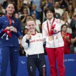 Maisie Summers-Newton at the medal ceremony of the individual medley holding up her gold medal alongside the ilver medallist Elizabeth Marks and bronze medallist Liu Daomin