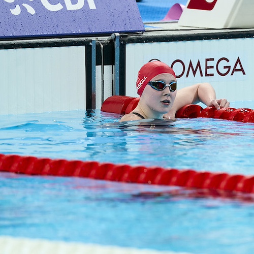 Poppy Maskill in the swimming pool wearing a red swim hat and goggles looking shocked with her mouth wide open after winning a gold medal