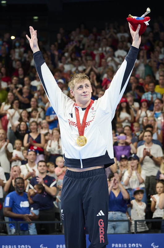 Stephen Clegg stood at the medal podium with his gold medal with his arms raised in celebration 